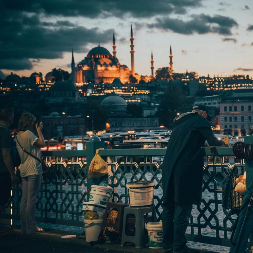 pexels-photo-7449446-7449446 Captured during twilight, the photo depicts people on Galata Bridge with Istanbul Mosque in the background, creating a vibrant city scene.